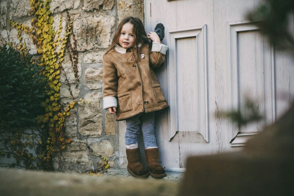 Enfant de maternelle en manteau d’automne et bottines devant une vieille porte